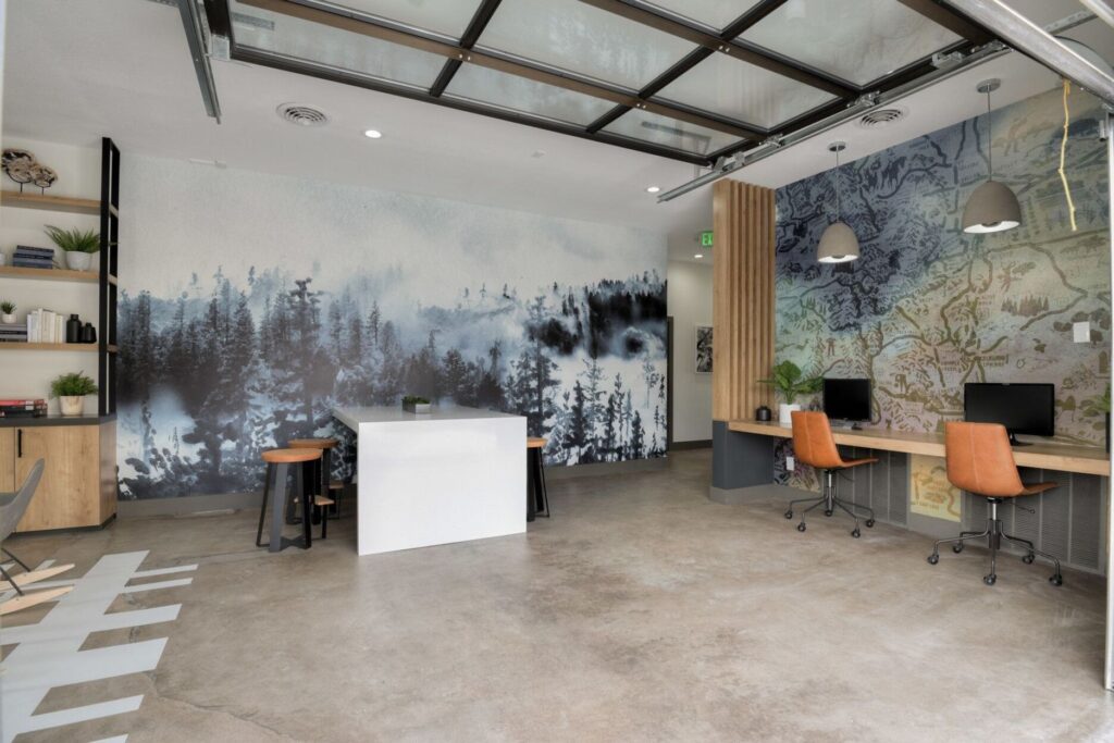 Clubhouse with business center area with table and stools. mural of foggy trees in the back and map on the wall to the right.